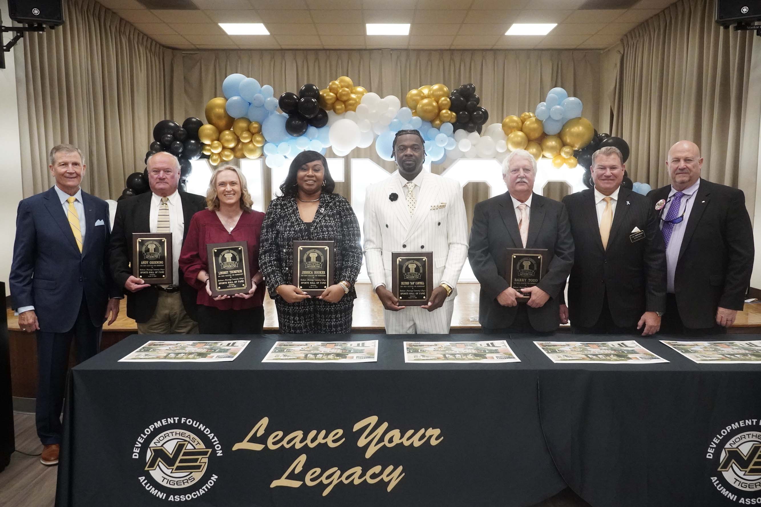 Group photo of award recipients and presenters at the Leave Your Legacy event, with a backdrop of black, gold, and blue balloons.