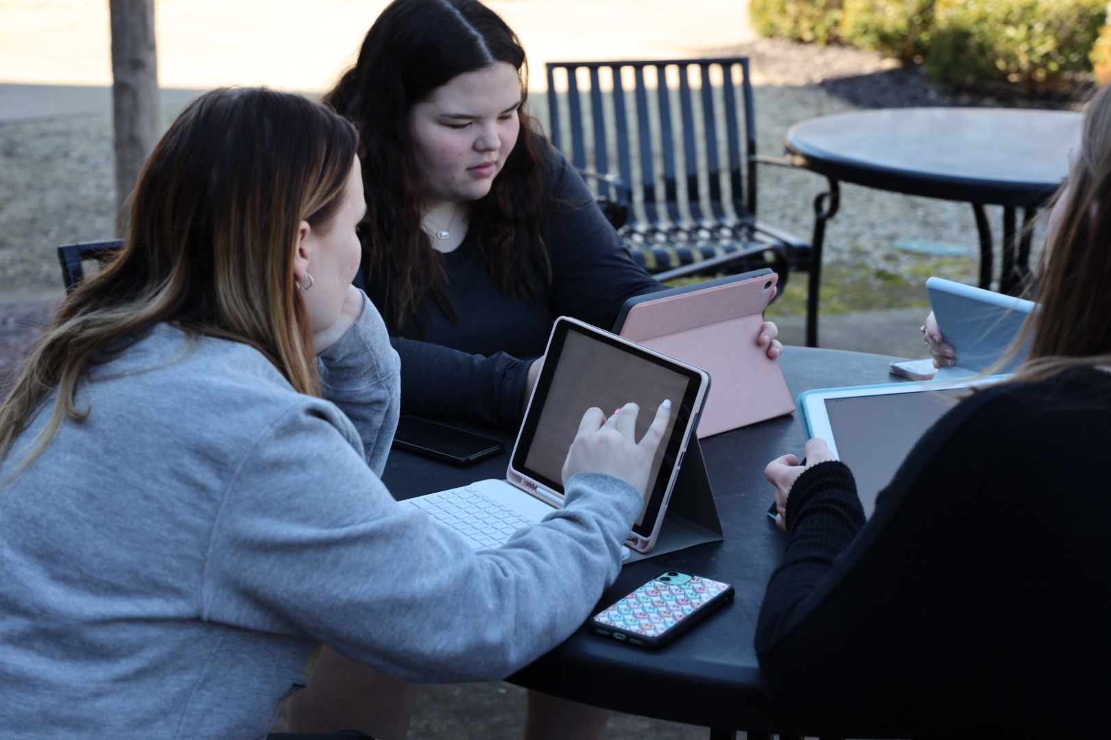 Three students sitting at a table using iPad