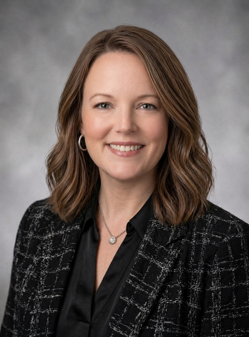 Female with light brown hair smiling at camera.  She is wearing a black blouse and gray blazer.