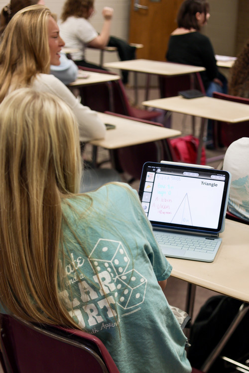 Photo of student in sitting in a desk with an iPad.  A math problem is displayed on the iPad.